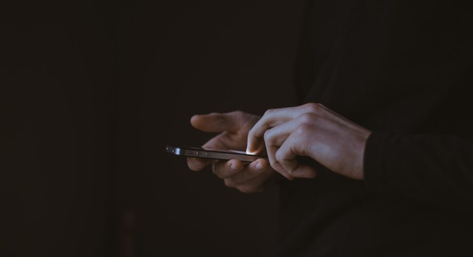 Two hands holding an iphone against a black background.