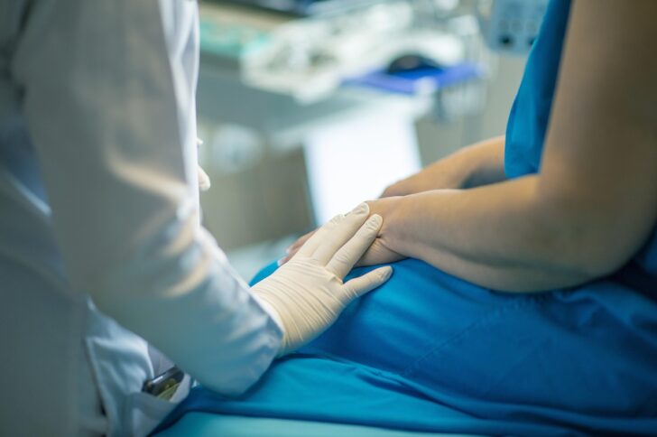 a health care provider with gloved hand touching a patient's arm