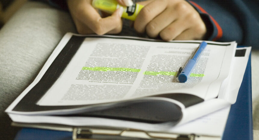 close-up of a woman's hand highlighting text on a paper.